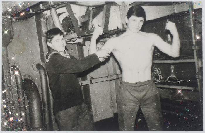 Two young men in a vintage photo, one flexing muscles, capturing moments from an impossibly normal life.