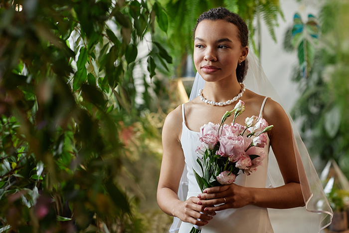 Bride holding a bouquet, standing amidst greenery at her wedding. Bride holding a bouquet, standing amidst greenery at her wedding.