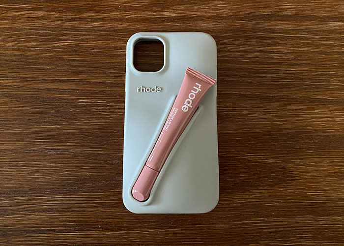 Expensive phone case with a pink lip product on a wooden surface. Expensive phone case with a pink lip product on a wooden surface.