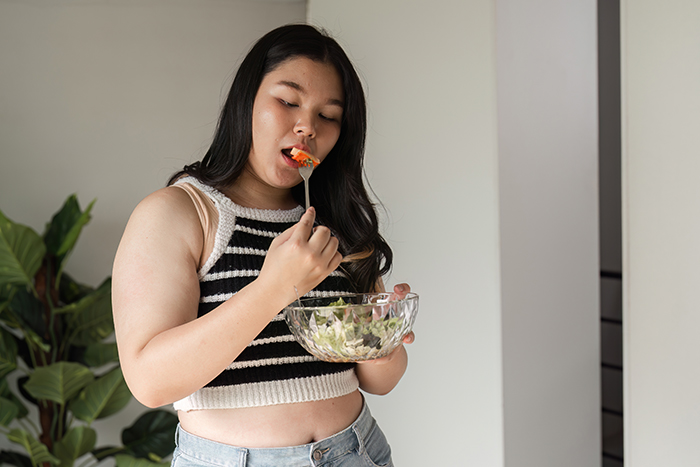 Woman eating salad indoors, representing backlash over grocery costs. Woman eating salad indoors, representing backlash over grocery costs.