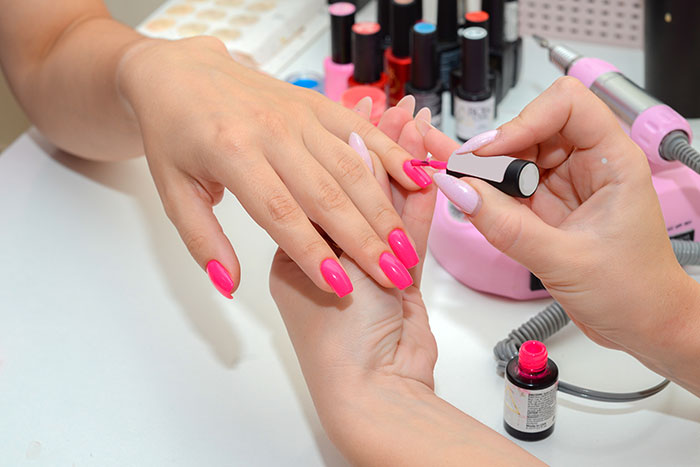 Woman getting bright pink nails painted at a nail salon, showcasing vibrant color options available. Woman getting bright pink nails painted at a nail salon, showcasing vibrant color options available.