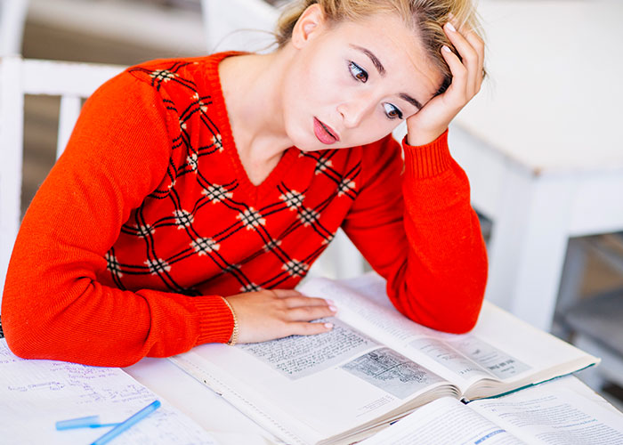 Student in red sweater looking stressed while studying at college library. Student in red sweater looking stressed while studying at college library.