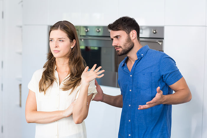 Man in blue shirt gestures, talking to woman in white shirt who looks away; tension over flaunting money. Man in blue shirt gestures, talking to woman in white shirt who looks away; tension over flaunting money.