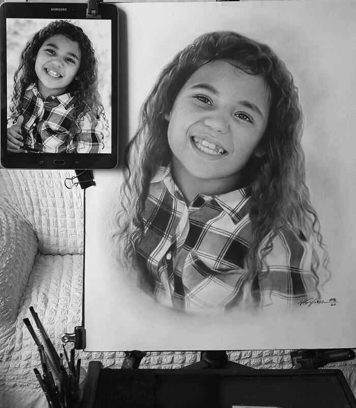 Hyper-realistic pencil portrait of a smiling child next to a reference photo on a tablet.