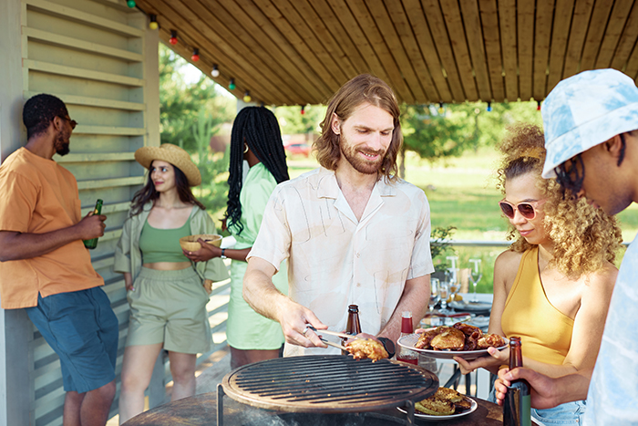 Man cooking gluten-free meal at a barbecue, surrounded by friends, outdoors under a wooden pergola. Man cooking gluten-free meal at a barbecue, surrounded by friends, outdoors under a wooden pergola.
