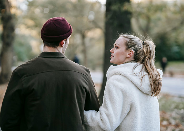 A man and woman walking in a park, engaging in a conversation, with trees in the background. A man and woman walking in a park, engaging in a conversation, with trees in the background.