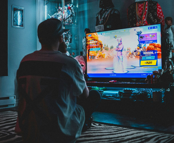 Person playing video games in a cozy room surrounded by collectibles, screen showing a playful game character. Person playing video games in a cozy room surrounded by collectibles, screen showing a playful game character.
