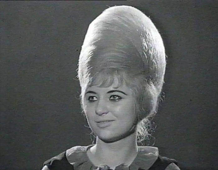 A woman with a towering, vintage hairstyle smiles in a classic black and white photo.