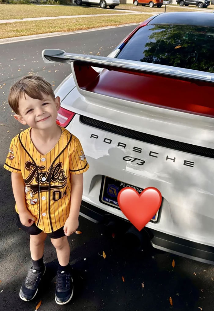 Smiling child standing next to a sports car with a large spoiler, enjoying a birthday surprise. Smiling child standing next to a sports car with a large spoiler, enjoying a birthday surprise.