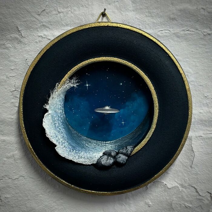 Alien-themed diorama with a UFO over a starry sky, enclosed in a circular frame with a wave and rocks.