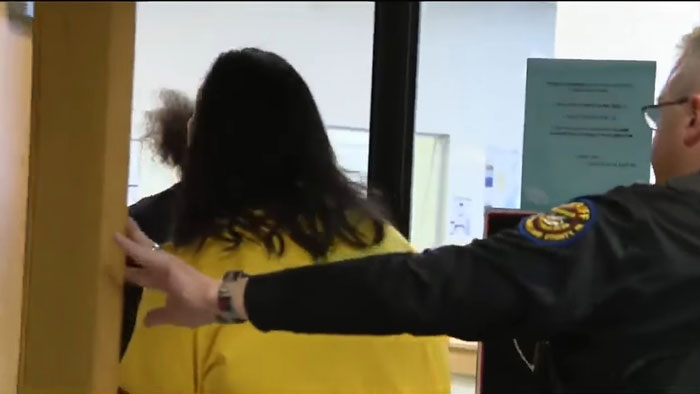 Officer escorts individual in yellow shirt, related to TikTok predator case, through a doorway in a secure area. Officer escorts individual in yellow shirt, related to TikTok predator case, through a doorway in a secure area.