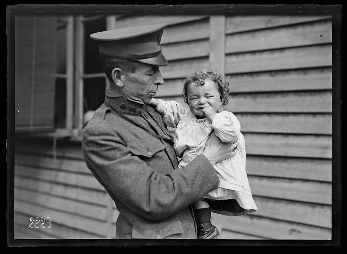 Man in vintage military uniform holding a toddler, a rare photograph rescued from glass negatives showing a historic moment.