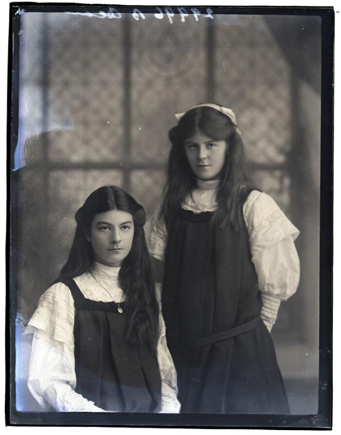 Two young women posed indoors in a rare photograph rescued from a glass negative with vintage clothing and hairstyles.