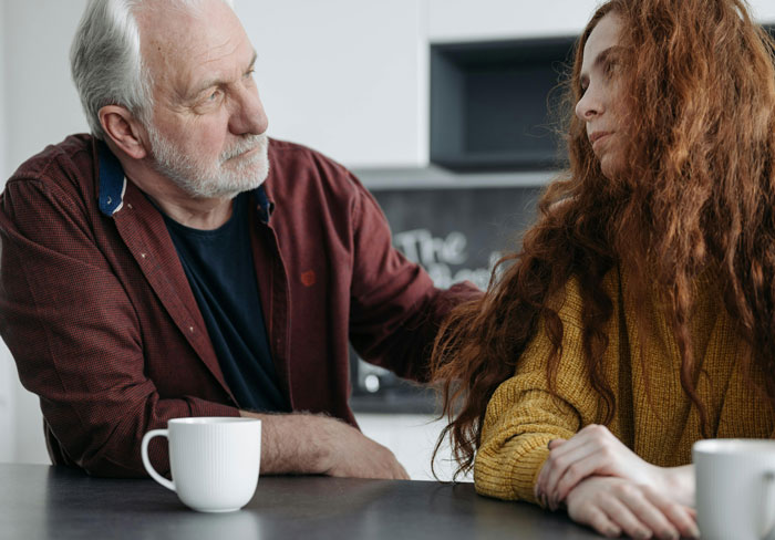 An older man and a younger woman sharing a meaningful conversation at a table, conveying emotions of love and surprise. An older man and a younger woman sharing a meaningful conversation at a table, conveying emotions of love and surprise.
