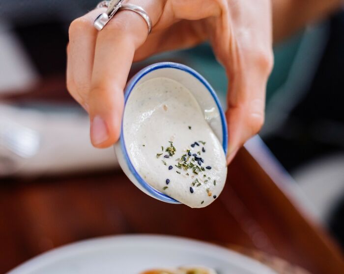 Person holding a small bowl of white sauce, highlighting American culinary habits that might seem unusual internationally.