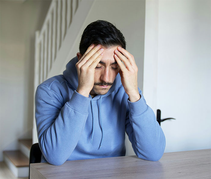 Man in blue hoodie with head in hands, feeling stressed about babysitting situation. Man in blue hoodie with head in hands, feeling stressed about babysitting situation.