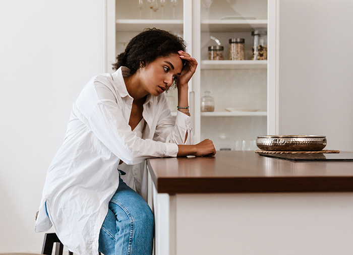 Woman sitting at kitchen counter, appearing thoughtful, wearing a white shirt and jeans, amid grocery-related dispute. Woman sitting at kitchen counter, appearing thoughtful, wearing a white shirt and jeans, amid grocery-related dispute.