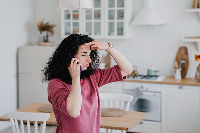 Woman on phone in kitchen, looking worried, discussing babysitting and play dates with another mom. Woman on phone in kitchen, looking worried, discussing babysitting and play dates with another mom.