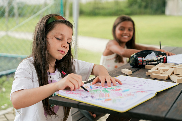 Two girls coloring at a picnic table, showcasing play date activities in an outdoor setting. Two girls coloring at a picnic table, showcasing play date activities in an outdoor setting.