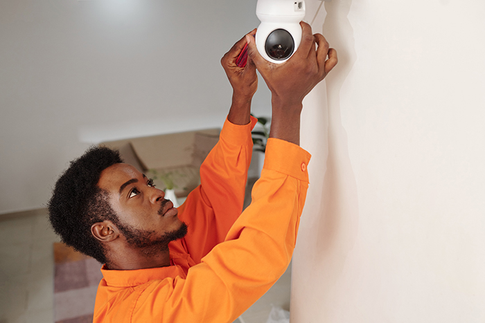 Man in orange shirt adjusting vacation house security camera indoors. Man in orange shirt adjusting vacation house security camera indoors.