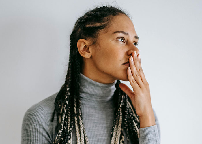 Woman in gray sweater looks pensive, hand covering mouth, reflecting on an anniversary date situation. Woman in gray sweater looks pensive, hand covering mouth, reflecting on an anniversary date situation.