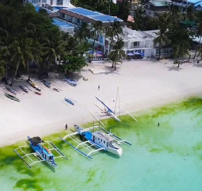Aerial view of a beach with anchored boats and nearby buildings, highlighting a serene travel location. Aerial view of a beach with anchored boats and nearby buildings, highlighting a serene travel location.