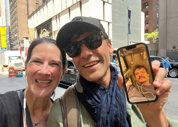 Two people smiling in the city, with one showing a video call on a smartphone featuring a celebrity.