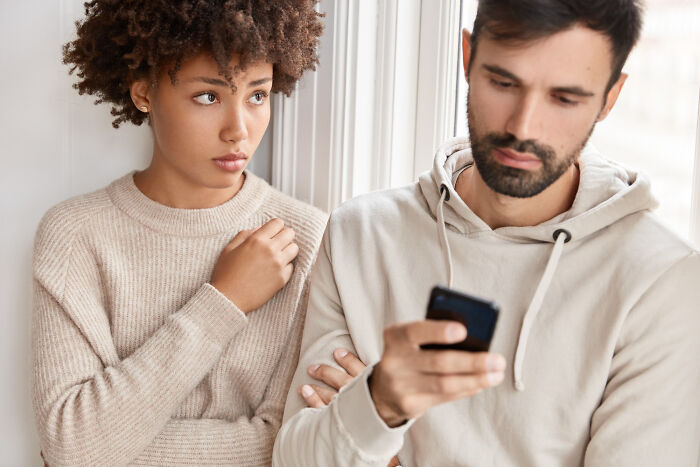 Worried woman looking at a man distracted by his phone, reflecting on why guys slept with a married woman.