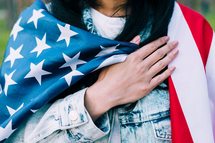 Person with an American flag, hand on heart, wearing a denim jacket, symbolizing patriotism.