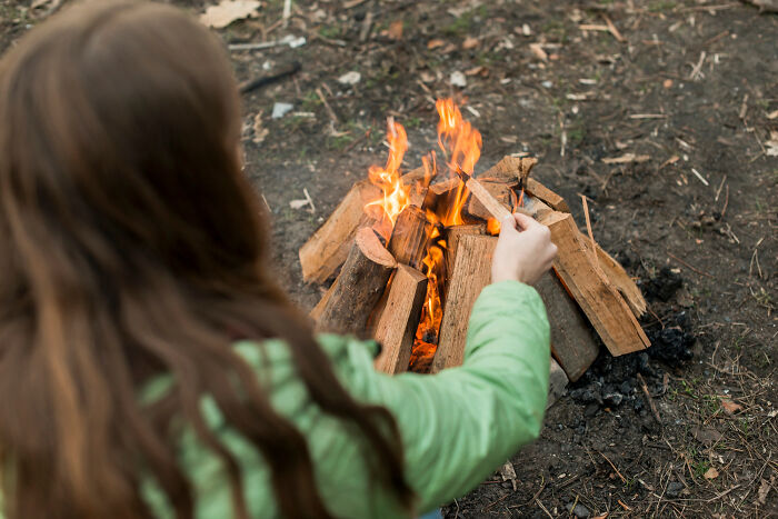 Woman tending to a campfire outdoors, challenging assumptions about women and survival skills.
