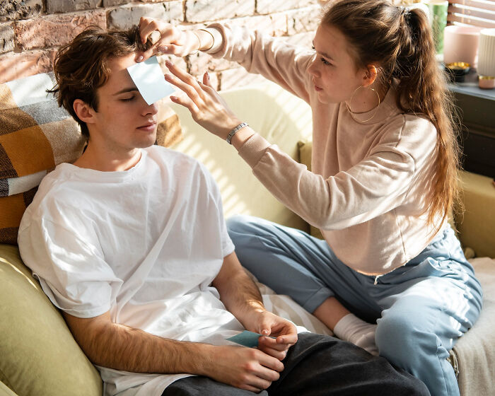 Woman placing a sticky note on man's forehead, illustrating dating dynamics and differences between men and women.