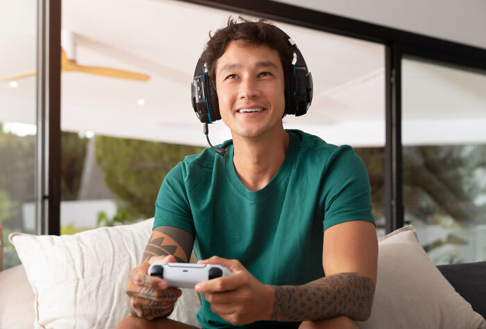 Man in a green shirt with headphones, smiling while gaming at home.