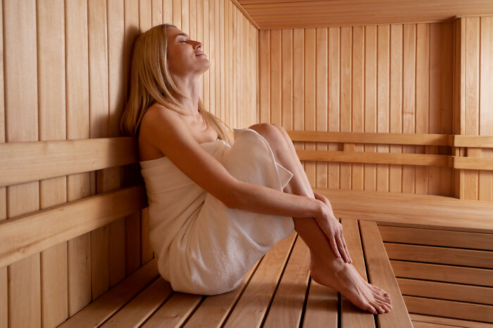 Woman wrapped in towel relaxing in a wooden sauna, enjoying a super normal thing country wellness routine.