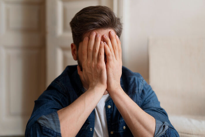 Man in denim shirt covering his face with hands, expressing distress on why guys slept with married woman.