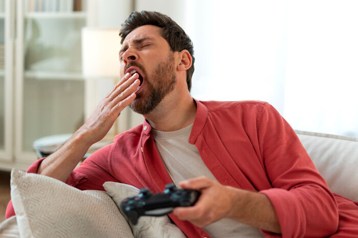 Man yawning on a couch, holding a game controller, illustrates unique male behavior in dating scenarios.