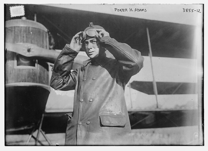 Vintage aviator adjusting goggles in front of an early aircraft, rare photographs rescued from glass negatives.