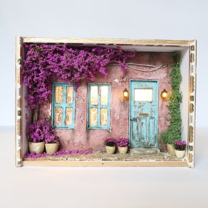 Miniature house facade with purple flowers and teal doors, showcasing detailed tiny world craftsmanship.