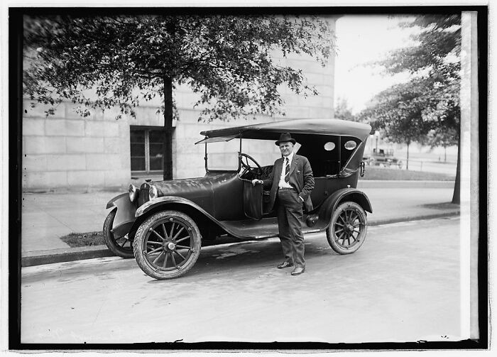Black and white vintage photograph restored from glass negatives showing a man standing beside an early 20th-century car.