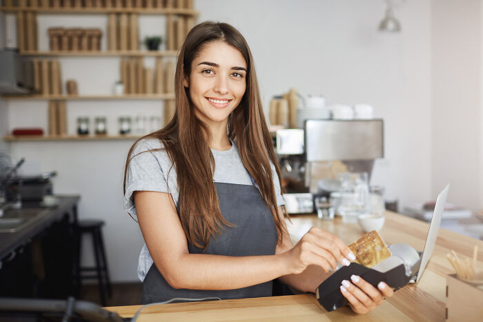 Woman smiling behind counter in coffee shop, challenging common assumptions about women.