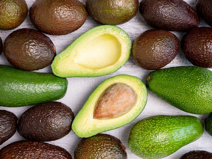 Avocados arranged on a wooden surface, with two halves showcasing the seed and flesh.