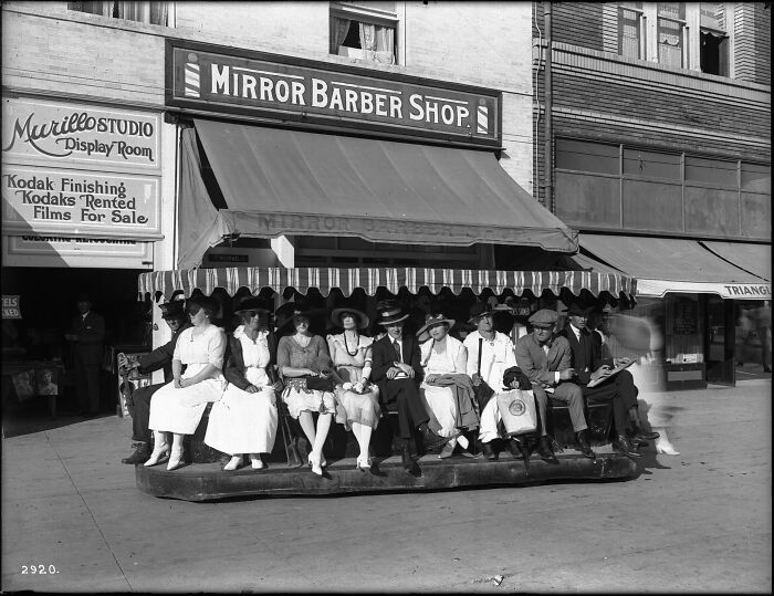 Group of people sitting outside Mirror Barber Shop in a rare photograph restored from glass negatives showing early 20th-century fashion.
