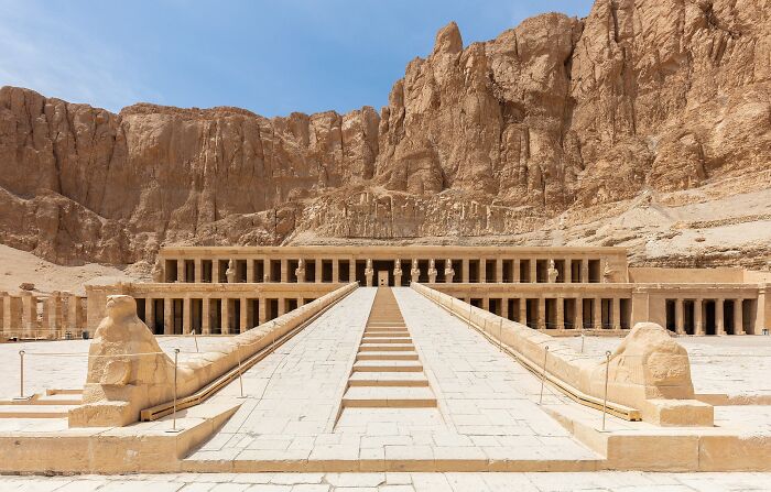 Ancient man-made structure of Hatshesut Temple in Egypt with stone columns set against rocky cliffs under a blue sky.