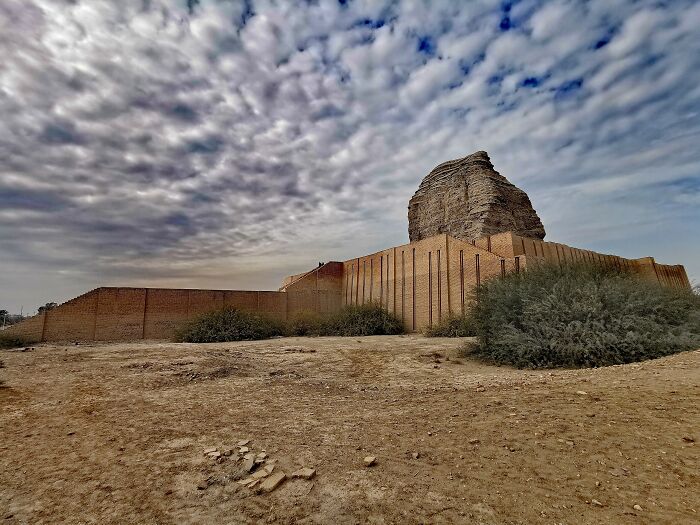 Ancient man-made structure with weathered brick walls and a large stone formation under a cloudy sky.