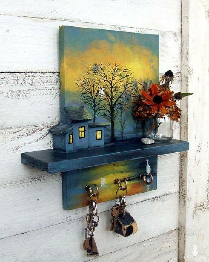 Woodworking project featuring a painted wooden shelf with key hooks, small house models, and a floral arrangement.