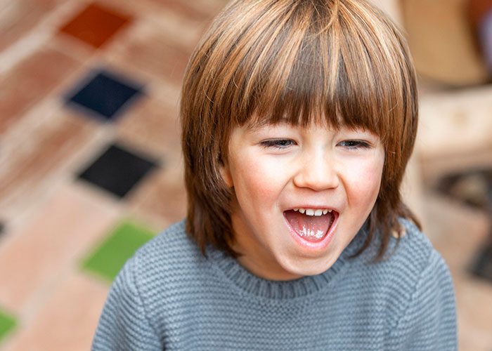 Three-year-old child with a joyful expression, wearing a gray sweater, in a colorful indoor setting. Three-year-old child with a joyful expression, wearing a gray sweater, in a colorful indoor setting.