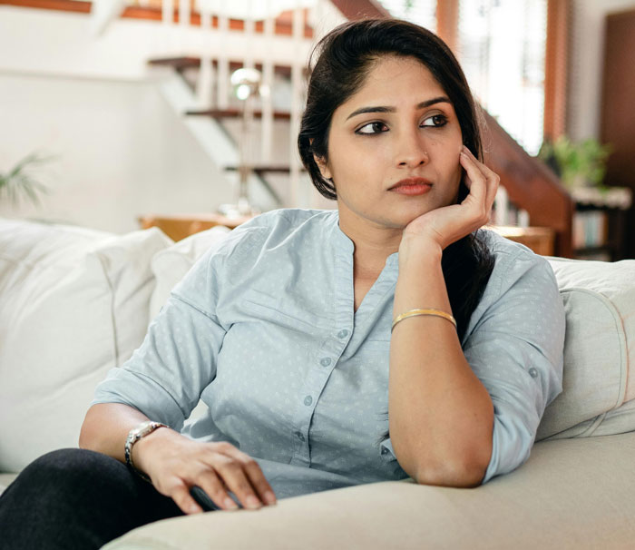 Woman looking concerned and thoughtful on a sofa, reflecting on MIL's baby comment. Woman looking concerned and thoughtful on a sofa, reflecting on MIL's baby comment.