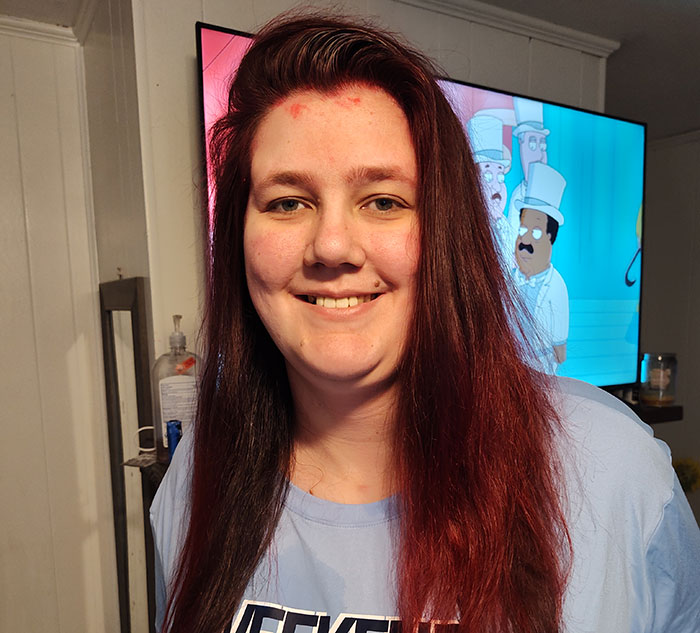 Smiling tall woman with long hair, standing indoors with a cartoon background on the TV. Smiling tall woman with long hair, standing indoors with a cartoon background on the TV.