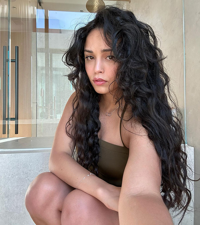 Streamer posing indoors with long curly hair, wearing a green top, linked to 'Minecraft' scene controversy. Streamer posing indoors with long curly hair, wearing a green top, linked to 'Minecraft' scene controversy.