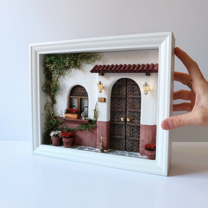 Miniature scene by Tamar Cohen depicting a detailed small house entrance with plants, framed and held in hand.