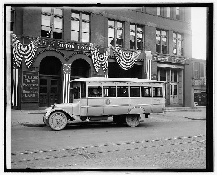 Rare photograph restored from glass negatives showing a vintage bus parked in front of decorated buildings.